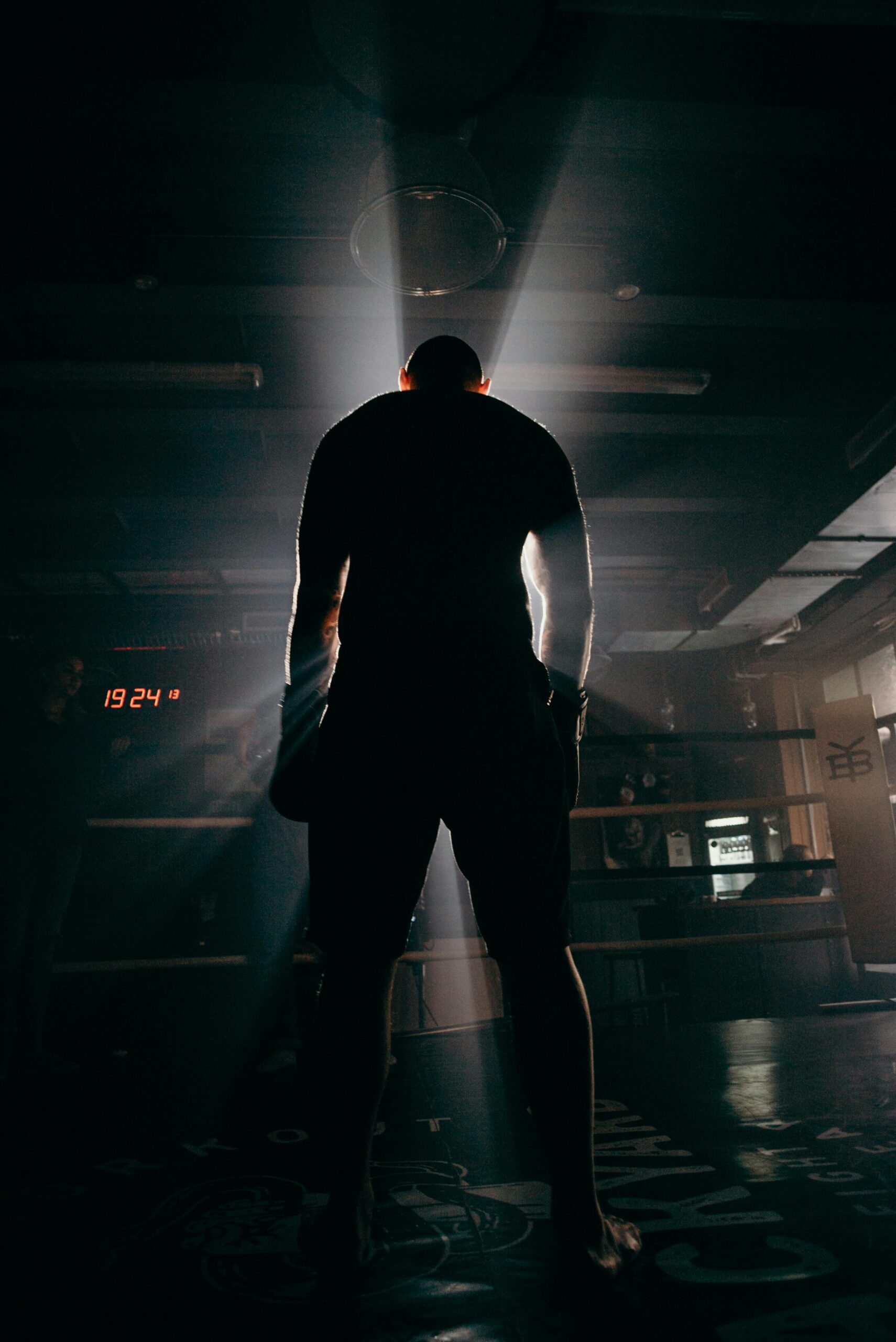 Silhouette of a boxer in a gym, illuminated by dramatic beams of sunlight, creating a powerful visual impact.